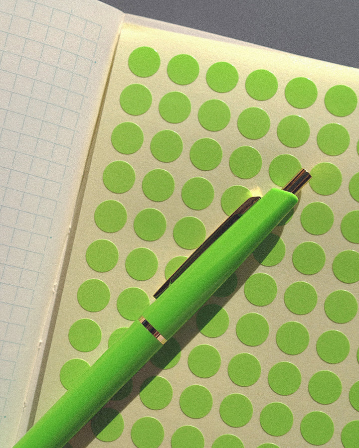 Anterique Lime Green Pen on top of some lime green spot stickers. Both are inside a grid notebook from Midori where you can see the brand's unique grid paper type.