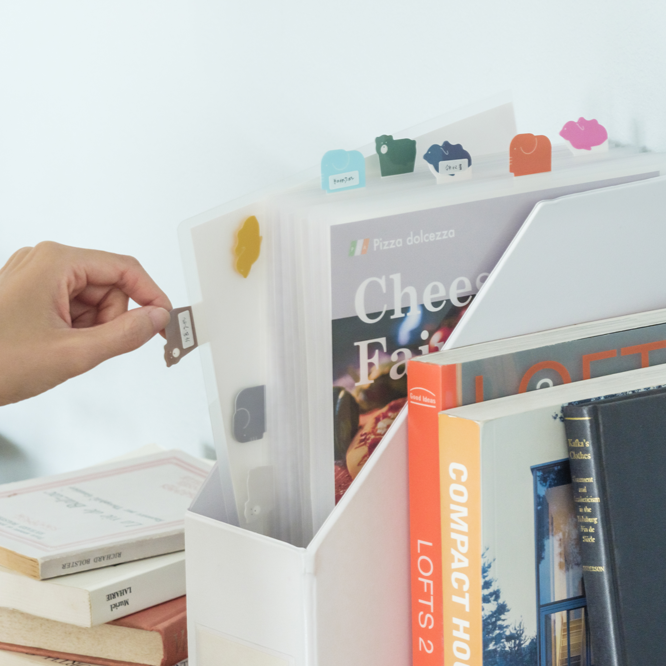 Hand placing a small item into a white magazine holder with books and colorful flags.