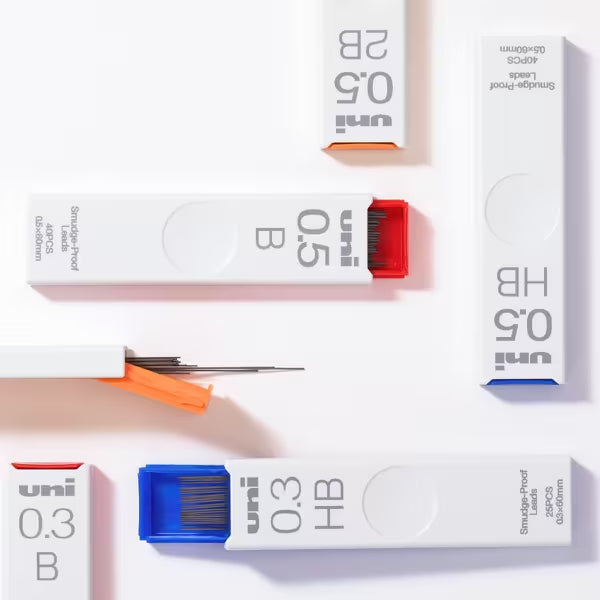 Several white Uni Smudge-proof Lead Refills cases are displayed on a light surface, each labeled with lead size and type. The graphite refills have blue, red, or orange caps for easy identification.