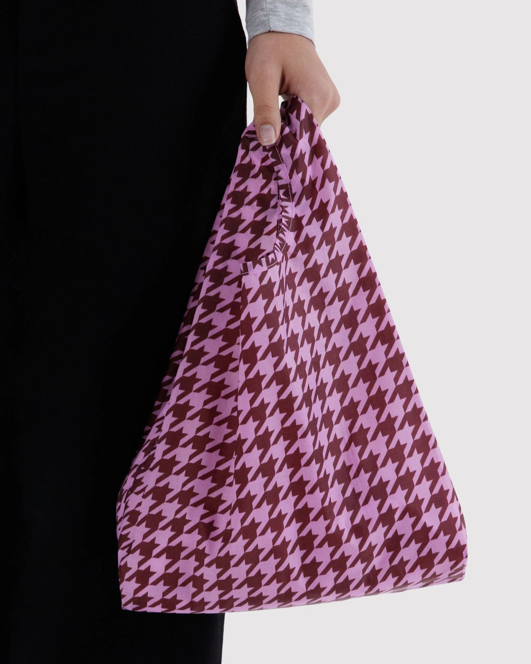 A person holding a large houndstooth pattern tote bag in pink and dark brown, shown against a light gray background.