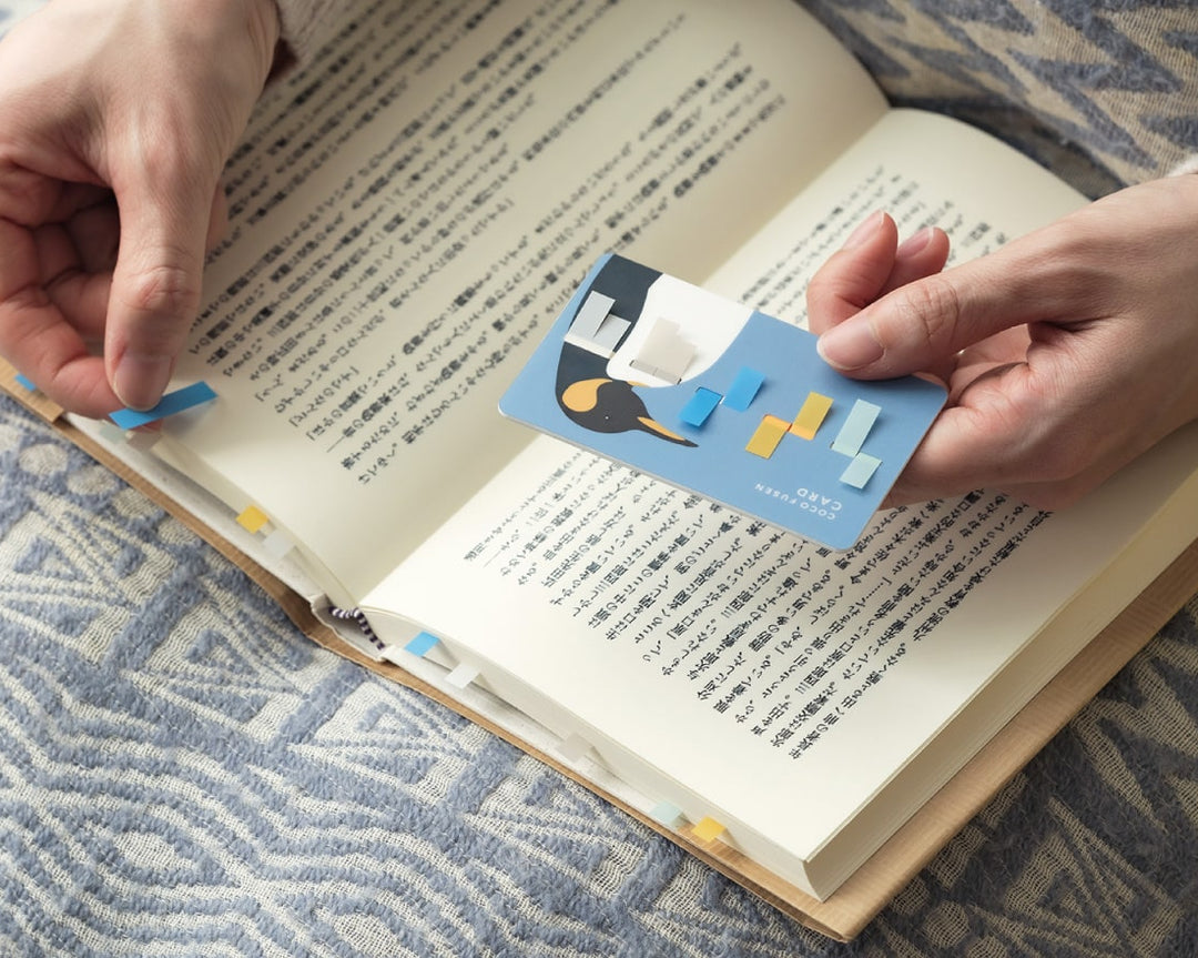 Person holding a small book or card next to an open book on a textured surface.