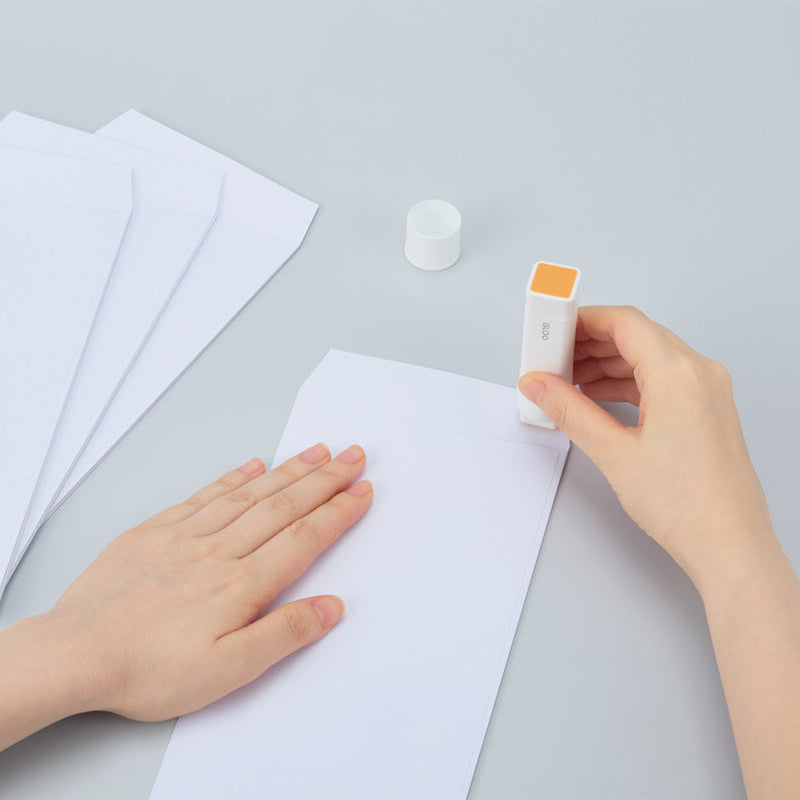 Person using a small device on a piece of paper with additional sheets and a bottle in the background.