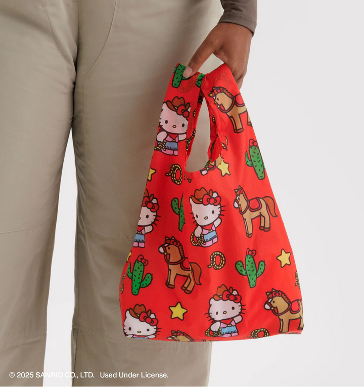 Red reusable bag with Hello Kitty and horse design held by a person wearing beige overalls.
