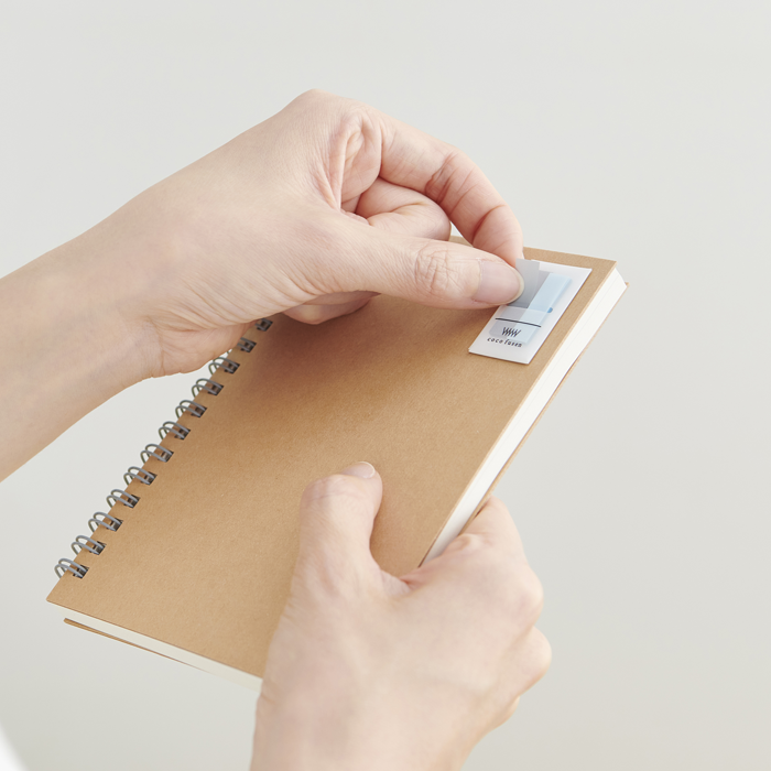 Person holding a beige notebook with a spiral binding on a light gray background